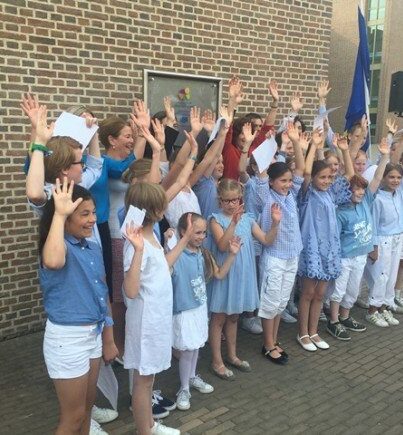 Minister Van Engelshoven (in het rood) gaat bijna verscholen achter het kinderkoor dat de bijeenkomst extra zonnig maakte