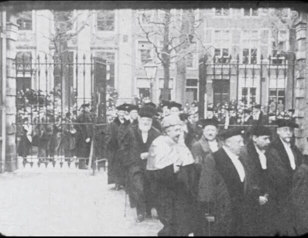 Albert Einstein draagt zijn toga van de universiteit van Berlijn met daarover de kappa van de universiteit van Madrid. Naast hem loopt Ehrenfest