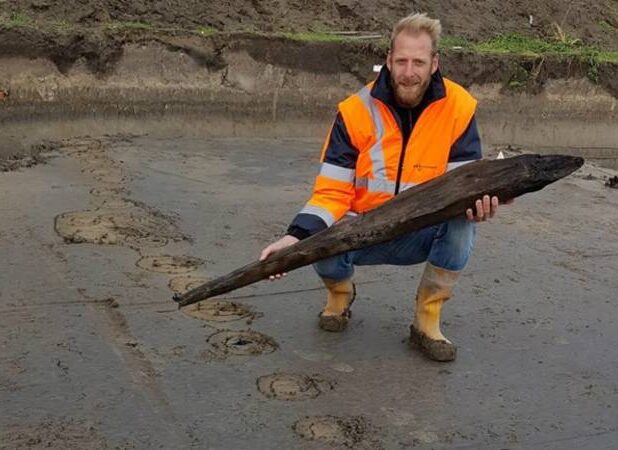 Een archeoloog toont een houten stut van de Romeinse weg bij Katwijk