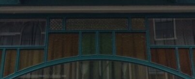 Detail met bovenlichten van winkelpui Lange Mare 53. Naast het gekleurde glas zijn drie ruitjes met ventilatieglas zichtbaar